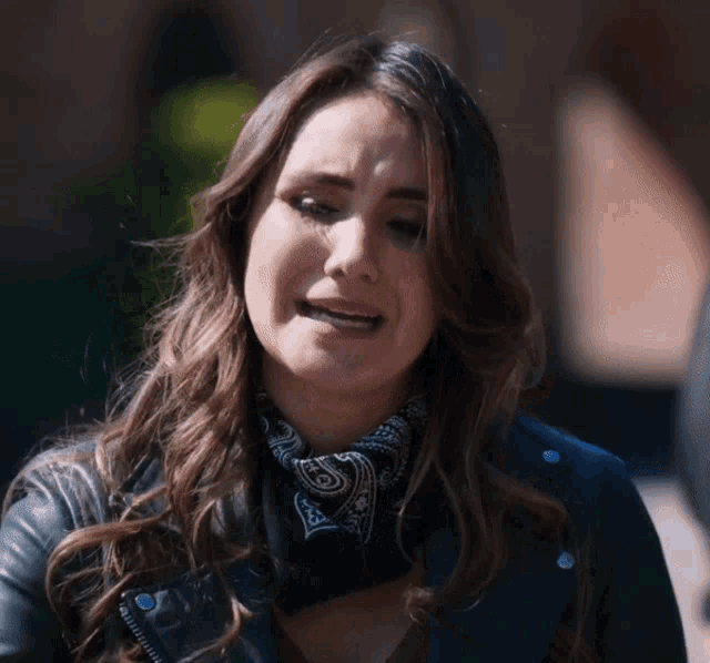 a woman wearing a bandana and a leather jacket makes a sad face
