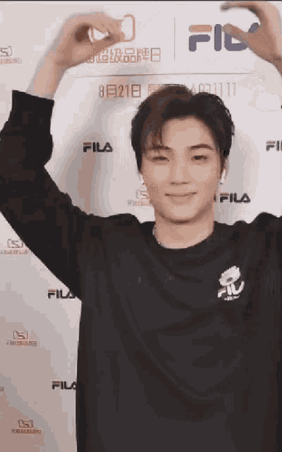 a man is making a heart shape with his hands while wearing a fila shirt