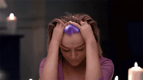 a woman in a purple shirt holds her head with her hands