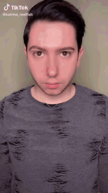a young man with a nose ring is wearing a gray shirt