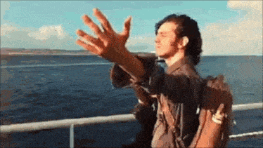 a man with a backpack is standing on a boat waving his hands in the air .