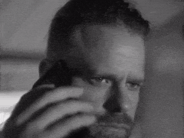 a black and white photo of a man with a beard talking on a cell phone .