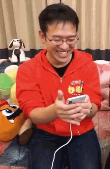 a man wearing glasses and a red sweatshirt with the number 8 on it is smiling while looking at his phone