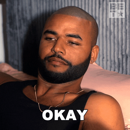 a man with a beard is laying on a bed with okay written on his face