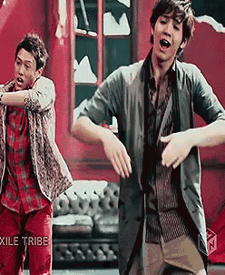 two men are dancing in front of a red wall with the word exile tribe on the bottom right