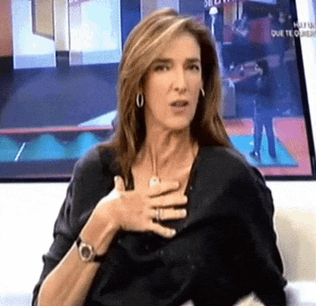 a woman is sitting on a couch with her hand on her chest in front of a screen that says que te quiero