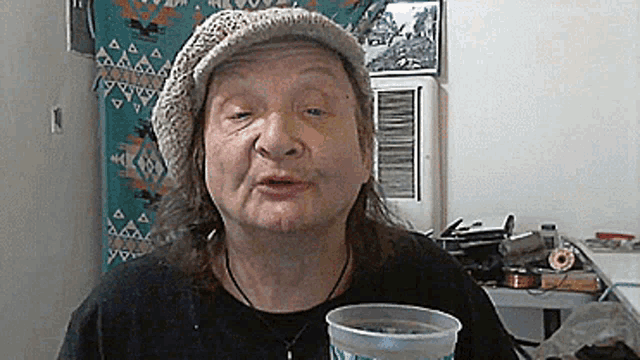 an elderly woman wearing a hat and holding a cup