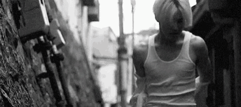 a black and white photo of a man in a tank top walking down a street .