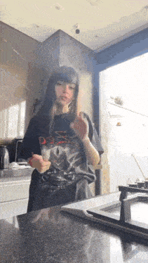 a girl in a black t-shirt is standing in a kitchen next to a stove .