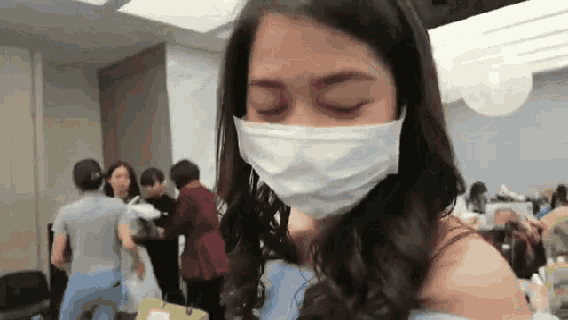 a woman wearing a face mask is standing in a room with people .