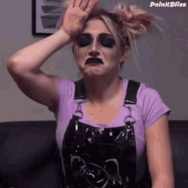 a woman in overalls is making a funny face while holding her hand to her forehead .