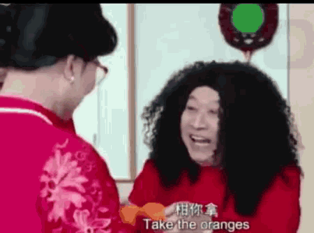 a man in a wig is talking to another man in a red shirt who is holding oranges .