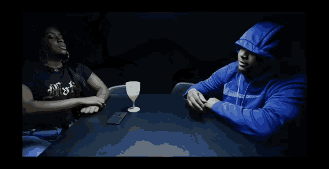 a man in a blue hoodie sits next to a woman in a black shirt