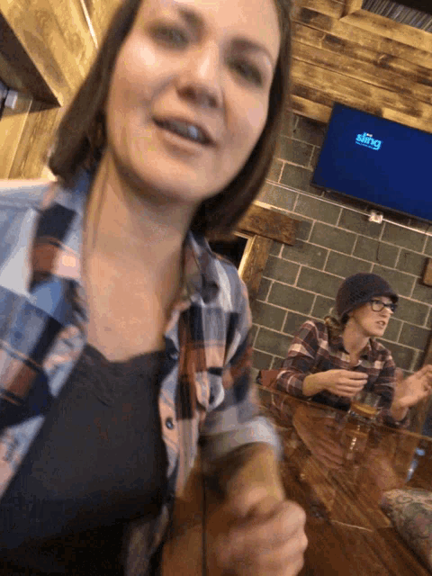 a woman in a plaid shirt is sitting at a table in front of a tv that says sling