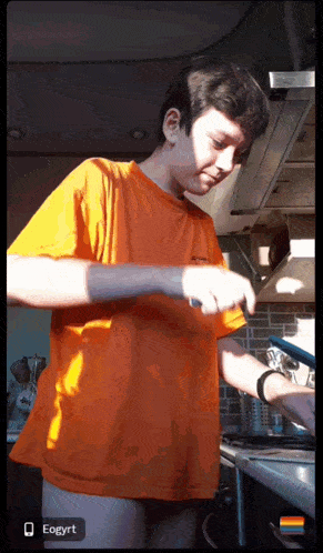 a boy in an orange shirt is cooking in the kitchen