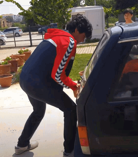 a man in a red and black sweatshirt is standing next to a car