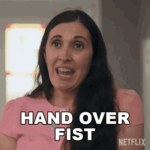 a woman in a pink shirt is making a face and saying hand over fist