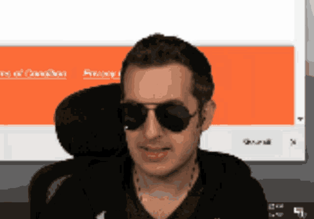 a man wearing sunglasses sits in front of a computer screen
