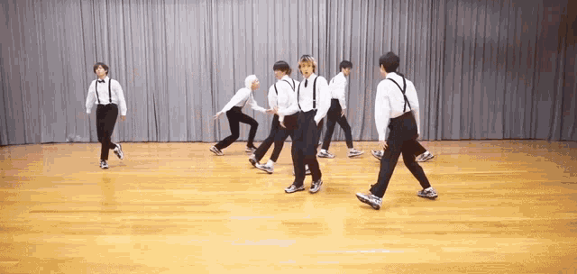 a group of young men in suspenders are dancing on a wooden floor