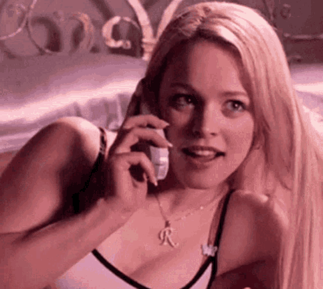 a woman is laying on a bed talking on a cell phone while wearing a necklace with the letter r on it .