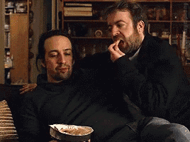 two men are sitting on a couch with a bowl of chips in front of them