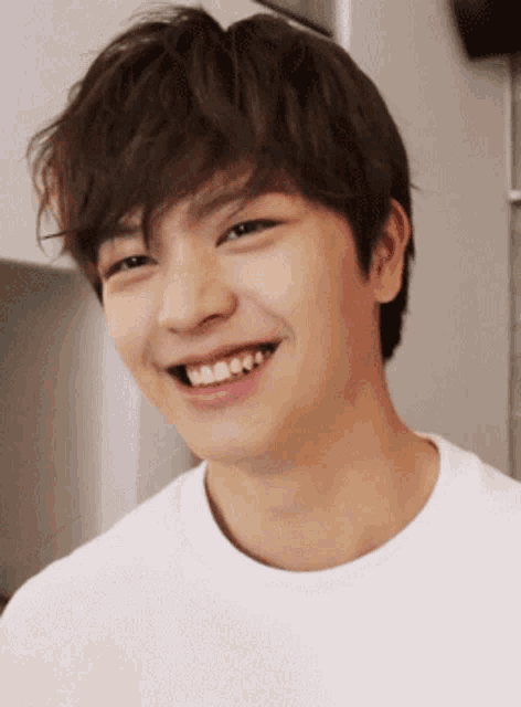 a young man wearing a white shirt is smiling and looking at the camera