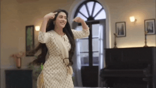 a woman in a white dress is dancing in a living room with her hands in her hair .