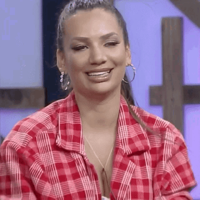 a woman is wearing a red plaid shirt and earrings and smiling .