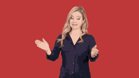 a woman in a blue shirt is making a funny face with her hands outstretched against a red background .