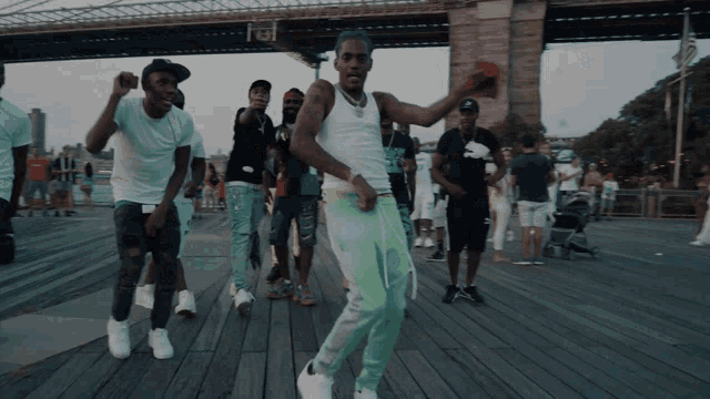 a group of young men are dancing on a boardwalk in front of a bridge
