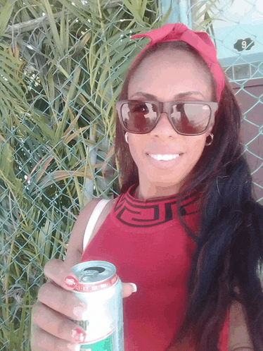 a woman wearing sunglasses and a red shirt holds a can of diet coke