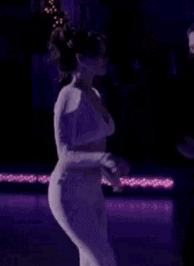a woman in a white top and white pants is dancing on a stage .