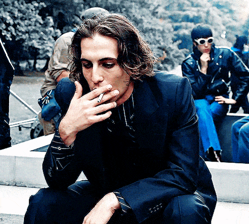 a man in a suit is smoking a cigarette while wearing sunglasses