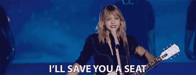 a woman singing into a microphone while holding a guitar and the words i 'll save you a seat