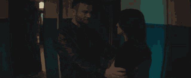 a woman wearing a black ellesse shirt stands in a dark room