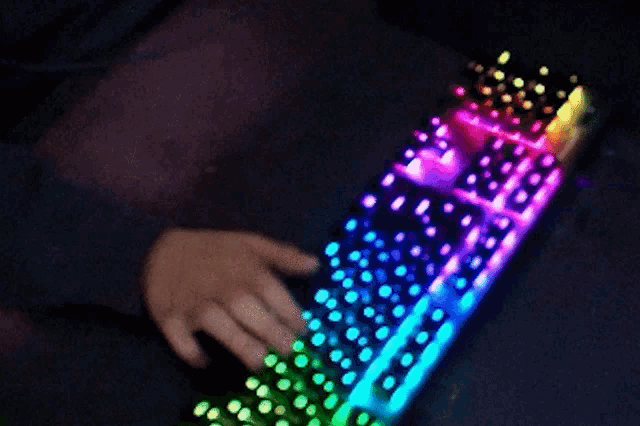 a person is typing on a keyboard that has a rainbow of lights on it