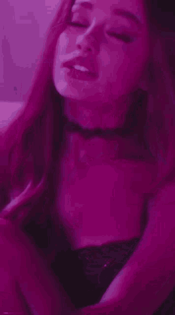 ariana grande is wearing a choker and a black top in a purple light .