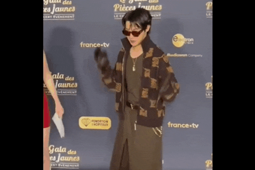 a man wearing sunglasses stands on a red carpet in front of a wall that says gala des jaunes on it