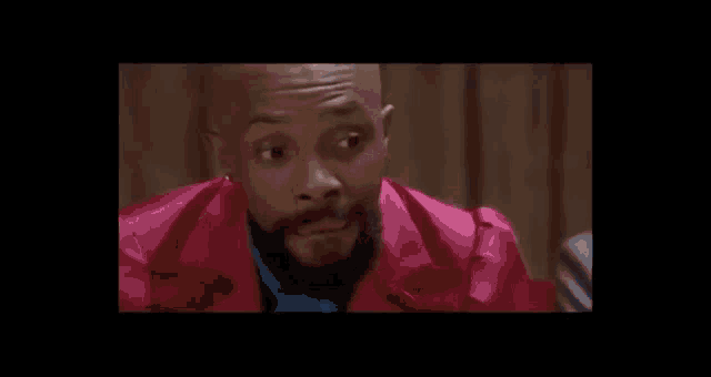 a man with a beard is smiling and wearing a pink jacket .