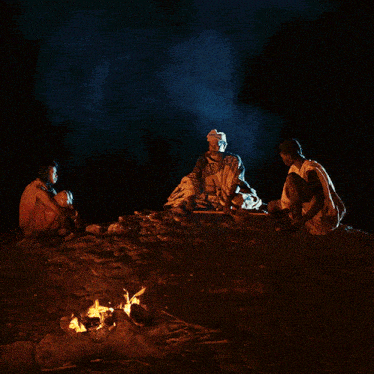 a group of people sitting around a fire in the dark