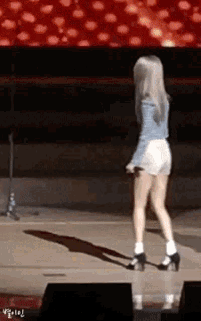a woman in a blue jacket and white shorts stands on a stage