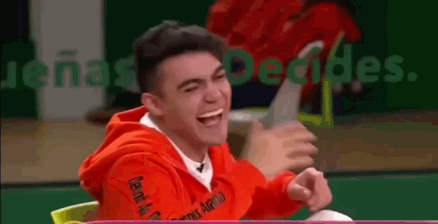 a young man in an orange hoodie is laughing while holding a tablet .
