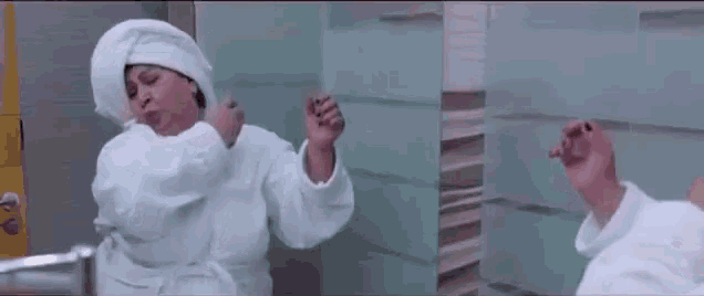 a woman in a bathrobe with a towel wrapped around her head is brushing her teeth .