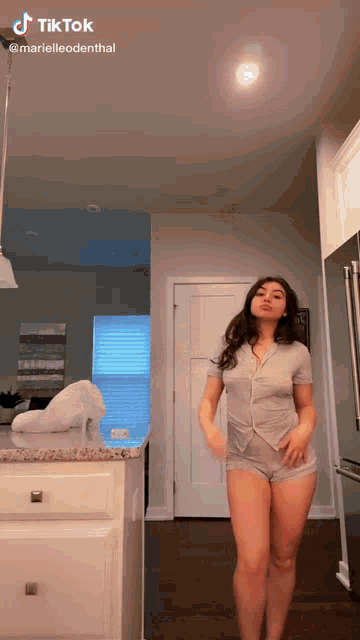 a woman is dancing in a kitchen wearing a gray shirt and shorts .