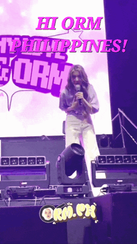a woman stands on a stage holding a microphone with the words hi orm philippines behind her