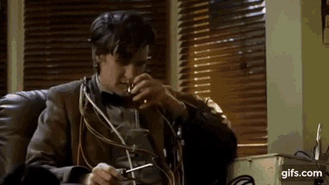 a man is sitting on a couch smoking a cigarette and drinking from a glass .