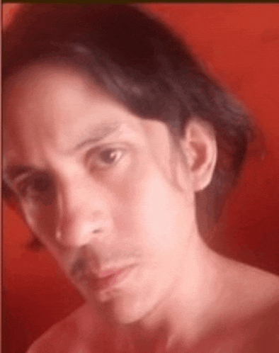 a man with long hair and a mustache is taking a selfie with a red background .
