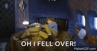 a man in a blue shirt is sitting on a couch with a lamp and says `` oh i fell over ! ''