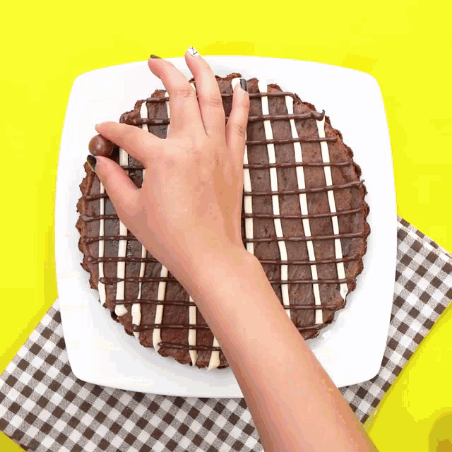 a person 's hand is reaching for a piece of chocolate cake on a plate