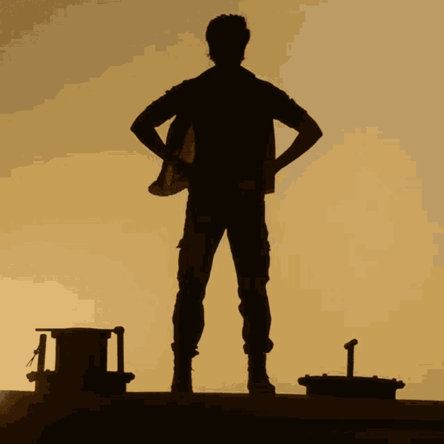 a silhouette of a man with his hands on his hips standing on a roof